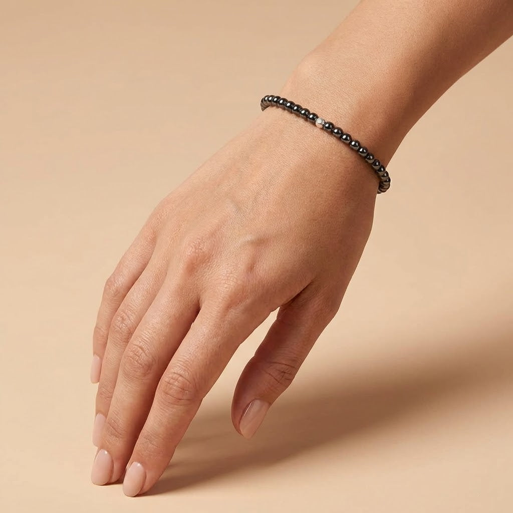 Hand wearing a black beaded bracelet on a beige background