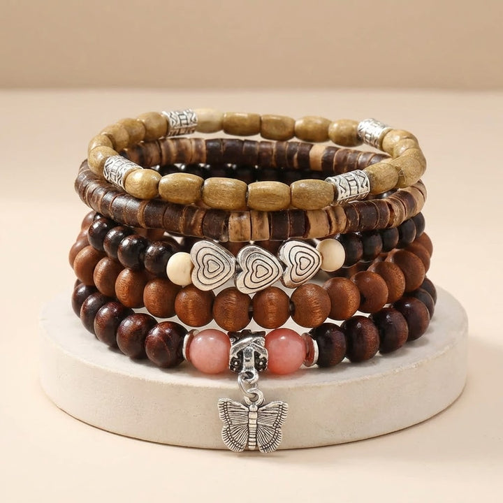 Stack of wooden beaded bracelets with heart and butterfly charms on a beige background