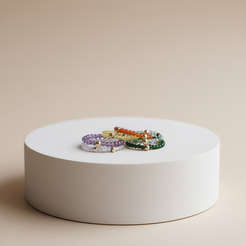 Three beaded bracelets on a white circular stand against a beige background