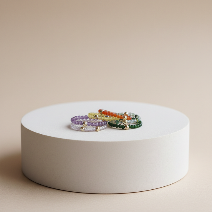 Three beaded bracelets on a white circular stand against a beige background