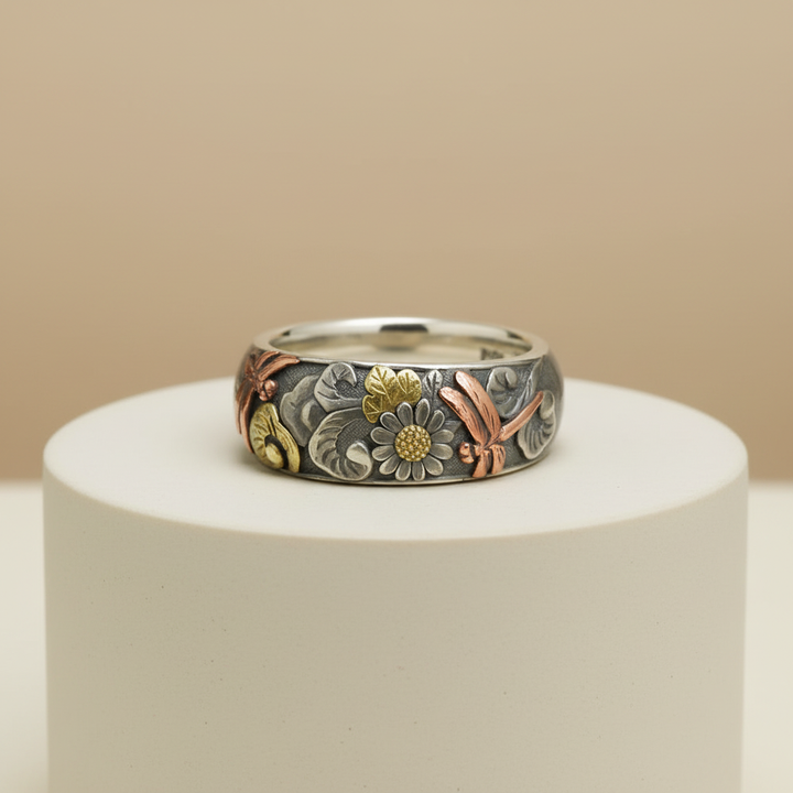 Silver ring with floral designs on a white pedestal against a beige background