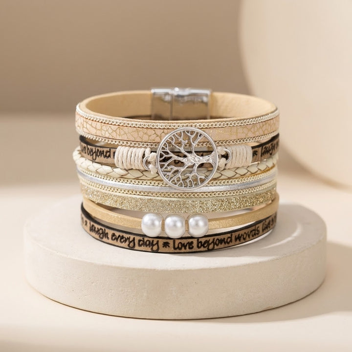 Stack of layered bracelets with tree of life design on a beige background